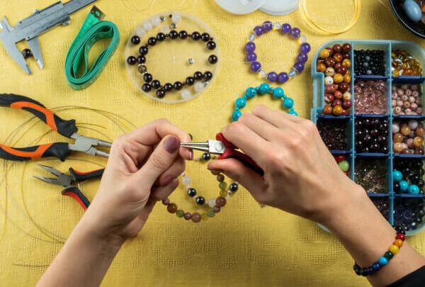 Jewelry making. Female hands with a tool on a yellow background.